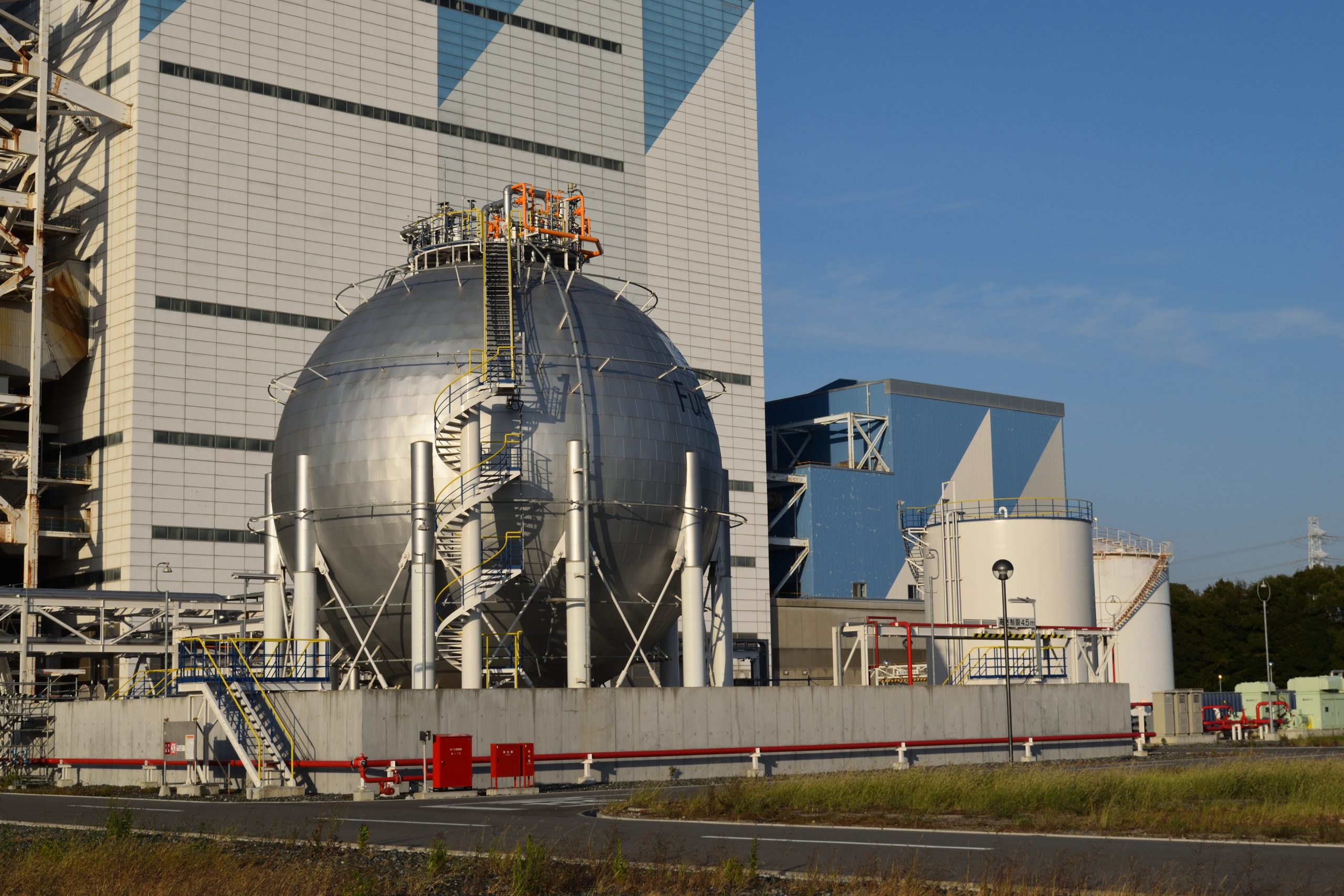 Ammonia tank used in the experiment. Ammonia is heavier than air and water-soluble, so the protective barrier and adjacent water tank form part of the leakage safety system. / アンモニアは空気より重く水に溶けやすいため、防護壁と隣接する水槽が漏えい時の安全システムとして機能します。